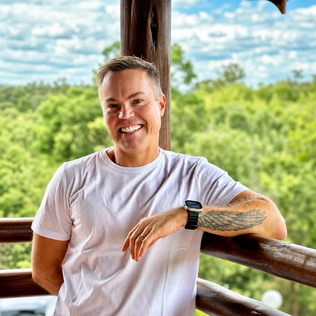 Osvaldo Beltramini sorrindo ao ar livre, apoiado em varanda com paisagem verde ao fundo.